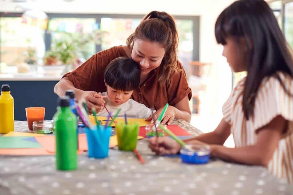 Asian Mother With Children Having Fun With Children Doing Craft On Table At Home